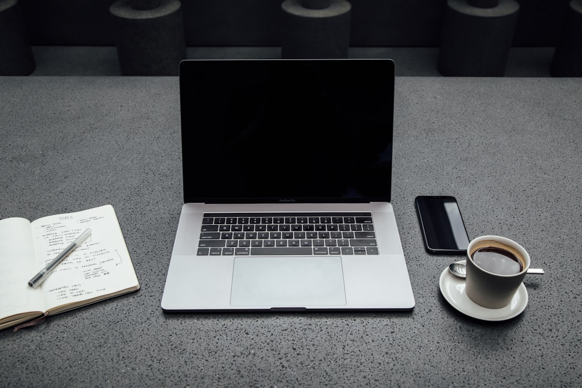 turned-off MacBook Pro between cup of coffee,