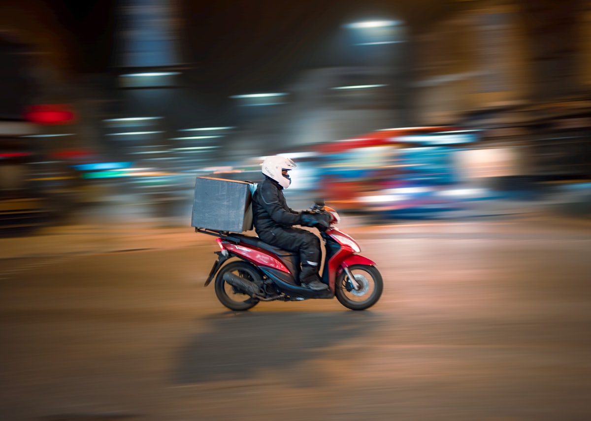 A delivery driver on a red scooter riding thr